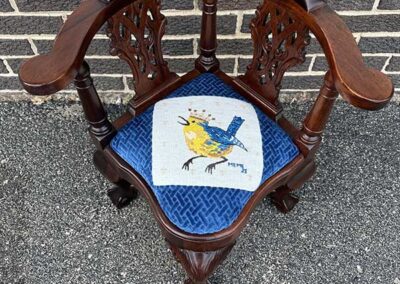 an antique three-legged chair with blue upholstery featuring a yellow bird wearing a crown