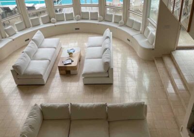 looking down on a dual white upholstered sofa set in a semi-circular room looking out on a pool